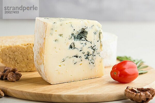 Blauschimmelkäse und verschiedene Käsesorten mit Rosmarin und Tomaten auf einem Holzbrett vor einem weißen Holzhintergrund. Seitenansicht  Nahaufnahme  selektiver Fokus