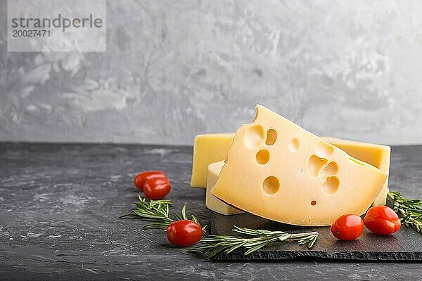 Verschiedene Käsesorten mit Rosmarin und Tomaten auf einer schwarzen Schiefertafel auf einem schwarzen Betonhintergrund. Seitenansicht  Nahaufnahme  Kopierraum  selektiver Fokus