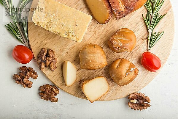 Geräucherter Käse und verschiedene Käsesorten mit Rosmarin und Tomaten auf einem Holzbrett auf einem weißen Holzhintergrund. Draufsicht  flach gelegt  Nahaufnahme
