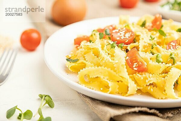 Reginelle Grießnudeln mit Tomaten  Eiern  Sesam und mikrogrünen Sprossen auf weißem Holzuntergrund und Leinenstoff. Seitenansicht  Nahaufnahme  selektiver Fokus