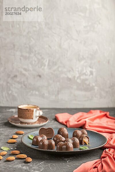 Schokoladenkaramellbonbons mit Mandeln und einer Tasse Kaffee auf einem schwarzen Betonhintergrund und rotem Textil. Seitenansicht  Kopierraum