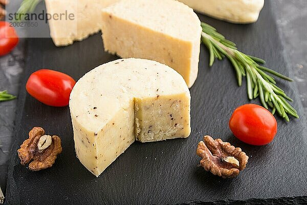 Cheddar Käse und verschiedene Käsesorten mit Rosmarin und Tomaten auf einer schwarzen Schieferplatte auf einem schwarzen Betonhintergrund. Seitenansicht  Nahaufnahme  selektiver Fokus