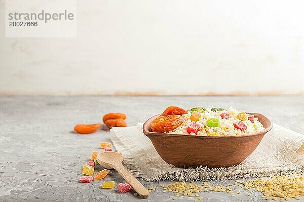 Bulgur Brei mit getrockneten Aprikosen und kandierten Früchten in einer Tonschüssel auf grauem Betonhintergrund und Leinentuch. Seitenansicht  Kopierraum  selektiver Fokus. Traditionelle türkische Küche