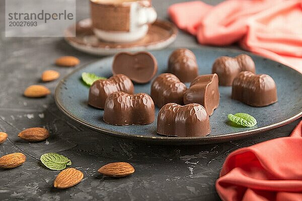 Schokoladenbonbons mit Mandeln und eine Tasse Kaffee auf einem schwarzen Betonhintergrund und rotem Textil. Seitenansicht  Nahaufnahme  selektiver Fokus