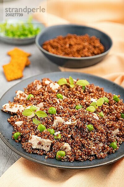 Quinoa Brei mit grünen Erbsen und Huhn auf Keramikteller auf grauem Betonhintergrund und orangefarbenem Textil. Seitenansicht  Nahaufnahme  selektiver Fokus