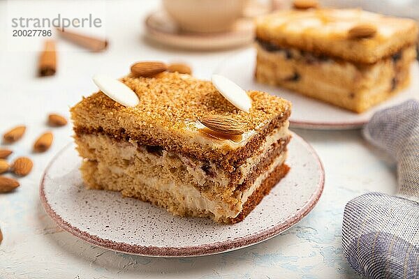 Honigkuchen mit Milchcreme  Karamell  Mandeln und einer Tasse Kaffee auf einem weißen Betonhintergrund und Leinenstoff. Seitenansicht  selektiver Fokus  Nahaufnahme