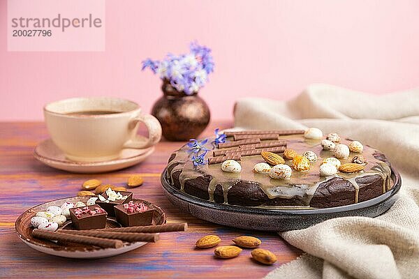 Hausgemachte Schokolade Brownie Kuchen mit Karamell Creme und Mandeln mit Tasse Kaffee auf einem farbigen und rosa Hintergrund und Leinen Textil. Seitenansicht  Nahaufnahme  selektiver Fokus