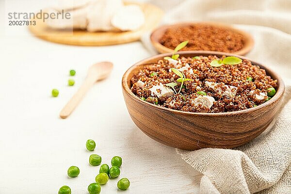 Quinoa Brei mit grünen Erbsen und Huhn in einer Holzschüssel auf einem weißen Holzhintergrund und Leinenstoff. Seitenansicht  Nahaufnahme  selektiver Fokus