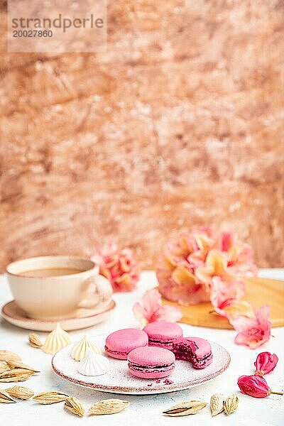 Lila Macarons oder Makronen Kuchen mit Tasse Kaffee auf einem weißen und braunen Beton Hintergrund mit Blumen verziert. Seitenansicht  Kopierraum  selektiver Fokus