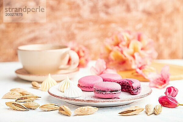 Lila Macarons oder Makronen Kuchen mit Tasse Kaffee auf einem weißen und braunen Beton Hintergrund mit Blumen verziert. Seitenansicht  Kopierraum  selektiver Fokus