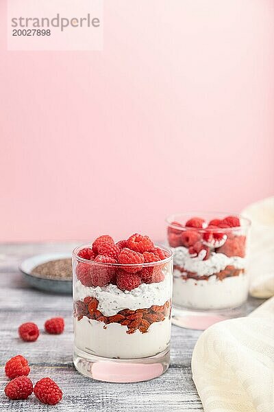 Joghurt mit Himbeeren  Goji Beeren und Chia Samen im Glas auf grauem und rosa Hintergrund und Leinenstoff. Seitenansicht  Kopierraum  selektiver Fokus