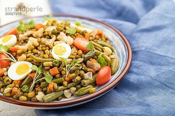 Mungobohnenbrei mit Wachteleiern  Tomaten und Mikrogrünsprossen auf weißem Betonhintergrund und blauem Textil. Seitenansicht  Nahaufnahme  selektiver Fokus