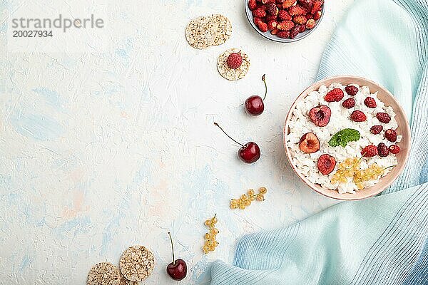 Reisflockenbrei mit Milch und Erdbeere in Keramikschüssel auf weißem Betonhintergrund und blauem Leinentextil. Draufsicht  flat lay  copy space