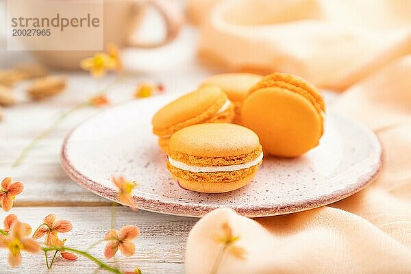 Orange Macarons oder Makronen Kuchen mit Tasse Aprikosensaft auf einem weißen hölzernen Hintergrund und orangefarbenen Leinen Textil. Seitenansicht  Nahaufnahme  selektiver Fokus