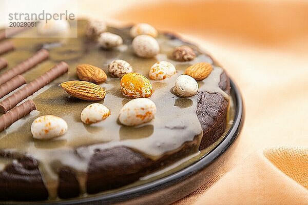 Hausgemachter Schokoladen Brownie Kuchen mit Karamellcreme und Mandeln mit einer Tasse Kaffee auf einem weißen Betonhintergrund und orangefarbenem Textil. Seitenansicht  Nahaufnahme  selektiver Fokus