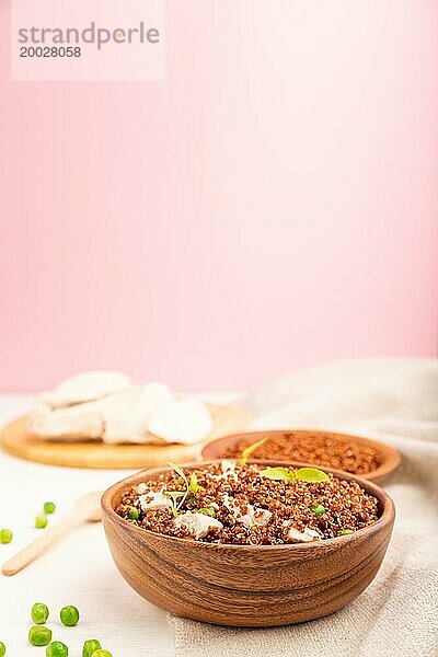 Quinoa Brei mit grünen Erbsen und Huhn in einer Holzschale auf weißem und rosa Hintergrund und Leinenstoff. Seitenansicht  Kopierraum  selektiver Fokus