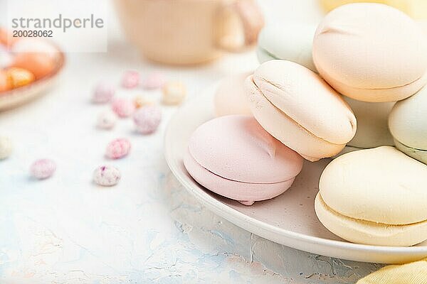 Farbiger Zephir oder Marshmallow mit Kaffeetasse und Dragees auf weißem Betonhintergrund und gelbem Textil. Seitenansicht  Nahaufnahme  selektiver Fokus