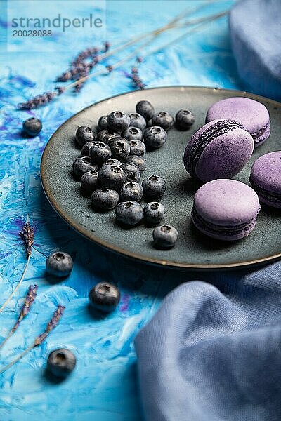 Lila Makronen oder Makronen Kuchen mit Blaubeeren auf Keramikteller auf einem blaün Beton Hintergrund und blaün Textil. Seitenansicht  Nahaufnahme  selektiver Fokus