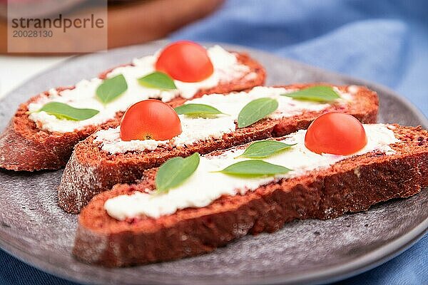 Rote Bete Brote mit Frischkäse und Tomaten auf weißem Betonhintergrund und blauem Leinentextil. Seitenansicht  selektiver Fokus  Nahaufnahme