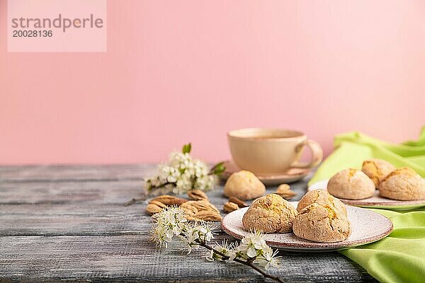 Mandelkekse und eine Tasse Kaffee auf grauem und rosa Hintergrund und grünem Leinenstoff. Seitenansicht  Nahaufnahme  selektiver Fokus  Kopierraum