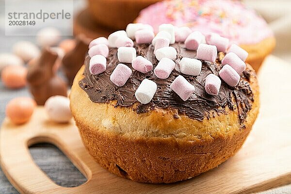 Hausgemachte glasierte und dekorierte Osterkuchen mit Schokoladeneiern und Kaninchen auf grauem Holzhintergrund und Leinentextil. Seitenansicht  selektiver Fokus  Nahaufnahme