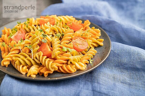 Tortiglioni Grießnudeln mit Tomaten und Mikrogrünsprossen auf einem schwarzen Betonhintergrund und blauem Textil. Seitenansicht  Nahaufnahme  selektiver Fokus