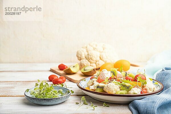 Vegetarischer Salat aus Blumenkohl  Kiwi  Tomaten  Mikrogrünsprossen auf weißem Holzhintergrund und blauem Leinentuch. Seitenansicht  Kopierraum  selektiver Fokus