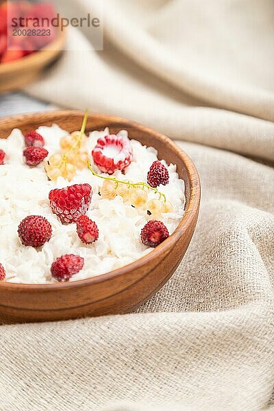 Reisflockenbrei mit Milch und Erdbeere in Holzschüssel auf grauem Holzhintergrund und Leinenstoff. Seitenansicht  selektiver Fokus  Nahaufnahme