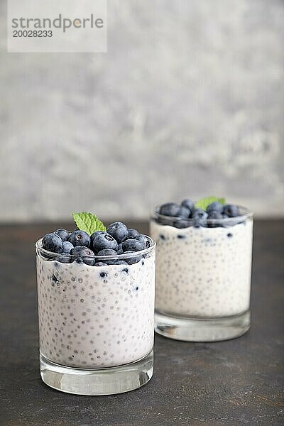 Joghurt mit Heidelbeeren und Chia im Glas auf schwarzem Betonhintergrund. Seitenansicht  Nahaufnahme  Kopierraum