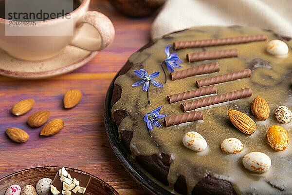 Hausgemachter Schokoladen Brownie Kuchen mit Karamellcreme und Mandeln mit einer Tasse Kaffee auf einem farbigen Holzhintergrund und Leinentuch. Seitenansicht  Nahaufnahme  selektiver Fokus