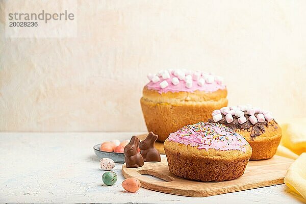 Hausgemachte glasierte und dekorierte Osterkuchen mit Schokoladeneiern und Kaninchen auf weißem Betonhintergrund und gelbem Textil. Seitenansicht  Kopierraum  selektiver Fokus