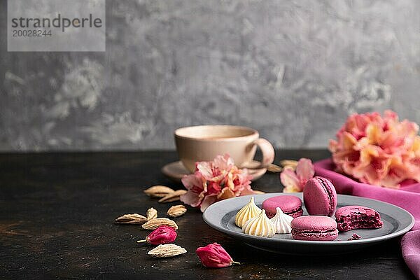 Lila Makronen oder Makronen Kuchen mit Tasse Kaffee auf einem schwarzen Beton Hintergrund und rosa Textil. Seitenansicht  Kopierraum  selektiver Fokus