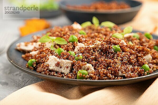 Quinoa Brei mit grünen Erbsen und Huhn auf Keramikteller auf grauem Betonhintergrund und orangefarbenem Textil. Seitenansicht  Nahaufnahme  selektiver Fokus