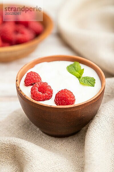 Joghurt mit Himbeeren in Tonbechern auf weißem Holzhintergrund und Leinentuch. Seitenansicht  Nahaufnahme  selektiver Fokus