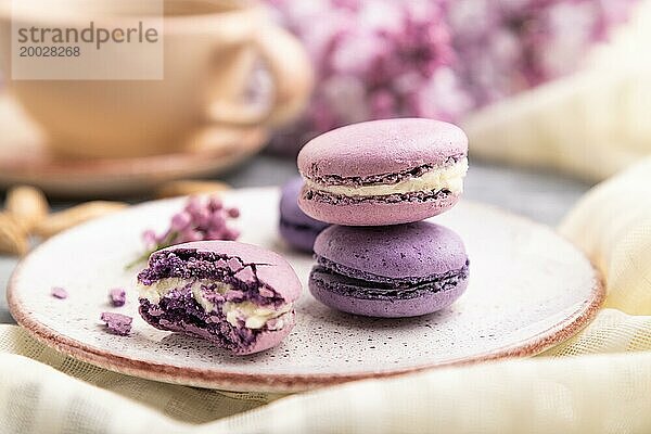 Lila Macarons oder Makronen Kuchen mit Tasse Kaffee auf einem grauen hölzernen Hintergrund und weißem Leinen Textil. Seitenansicht  Nahaufnahme  selektiver Fokus