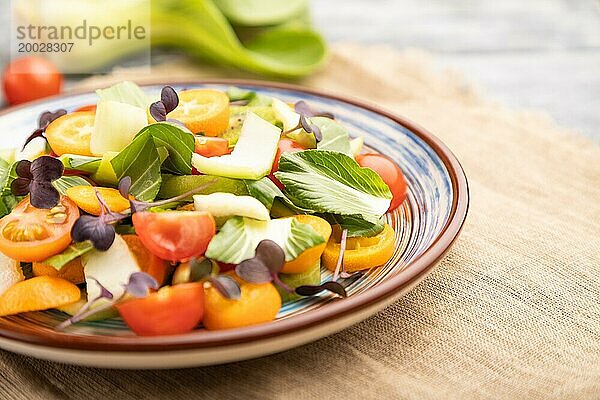 Vegetarischer Salat aus Pac Choi Kohl  Kiwi  Tomaten  Kumquat  Mikrogrünsprossen auf grauem Holzhintergrund und Leinentuch. Seitenansicht  Nahaufnahme  selektiver Fokus