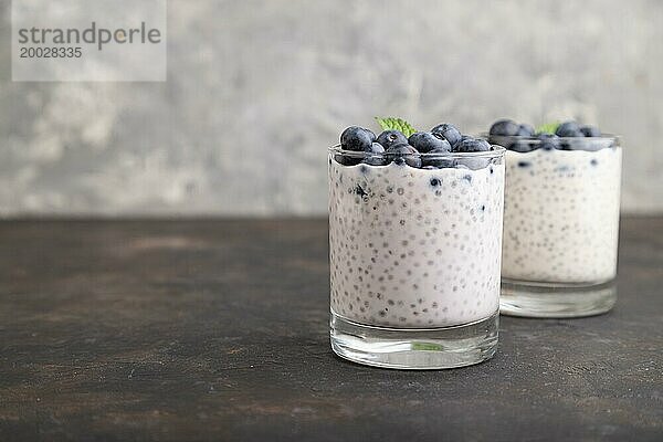 Joghurt mit Heidelbeeren und Chia im Glas auf schwarzem Betonhintergrund. Seitenansicht  Nahaufnahme  Kopierraum