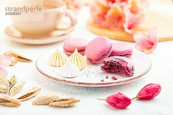 Lila Makronen oder Makronen Kuchen mit Tasse Kaffee auf einem weißen Beton Hintergrund mit Blumen verziert. Seitenansicht  Nahaufnahme  selektiver Fokus