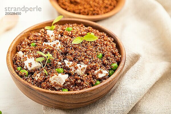 Quinoa Brei mit grünen Erbsen und Huhn in einer Holzschüssel auf einem weißen Holzhintergrund und Leinenstoff. Seitenansicht  Nahaufnahme  selektiver Fokus