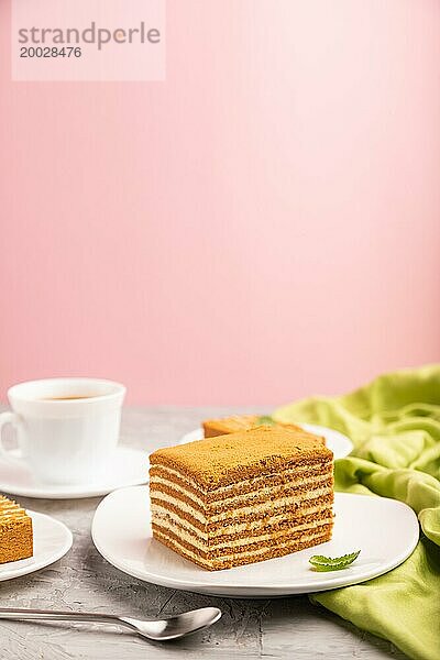 Hausgemachter Honigkuchen mit Milchcreme und Minze mit einer Tasse Kaffee auf einem rosa Hintergrund und grünem Textil. Seitenansicht  Kopierraum  selektiver Fokus