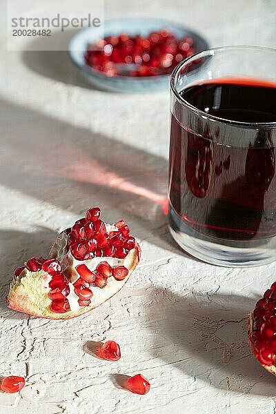 Glas Granatapfelsaft auf einem weißen Betonhintergrund. Hartes Licht  Kontrast. Seitenansicht  Nahaufnahme  selektiver Fokus