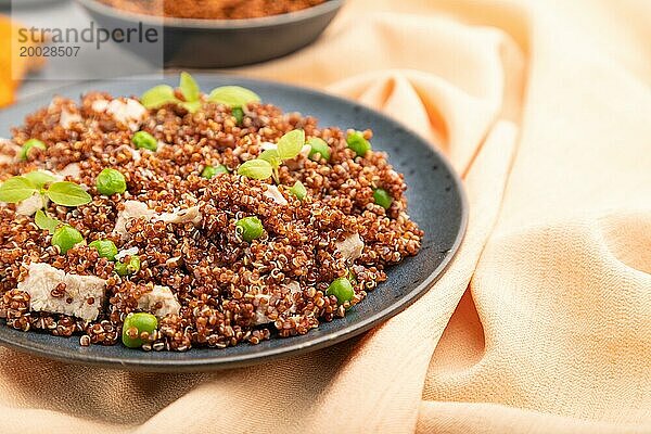 Quinoa Brei mit grünen Erbsen und Huhn auf Keramikteller auf grauem Betonhintergrund und orangefarbenem Textil. Seitenansicht  Nahaufnahme  selektiver Fokus