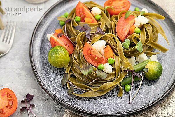 Tagliatelle mit grünem Spinat  Tomaten  Erbsen und Mikrosprossen auf grauem Betonhintergrund und Leinentuch. Seitenansicht  Nahaufnahme  selektiver Fokus