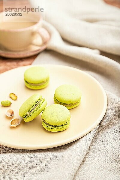 Grüne Macarons oder Makronen Kuchen mit Tasse Kaffee auf einem braunen Beton Hintergrund und Leinen Textil. Seitenansicht  Nahaufnahme  selektiver Fokus