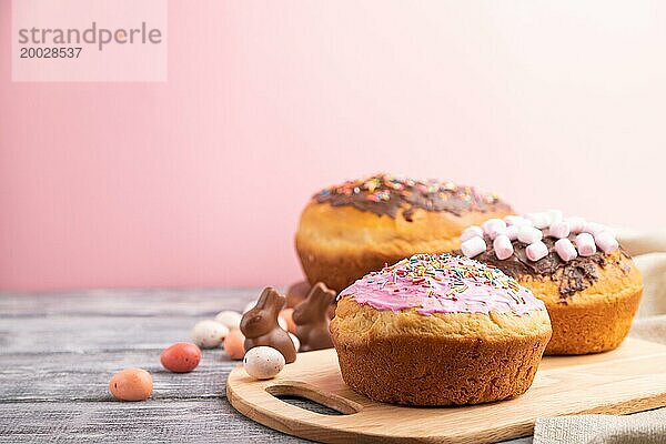 Hausgemachte glasierte und dekorierte Osterkuchen mit Schokoladeneiern und Kaninchen auf grauem und rosa Hintergrund und Leinenstoff. Seitenansicht  selektiver Fokus  Kopierraum