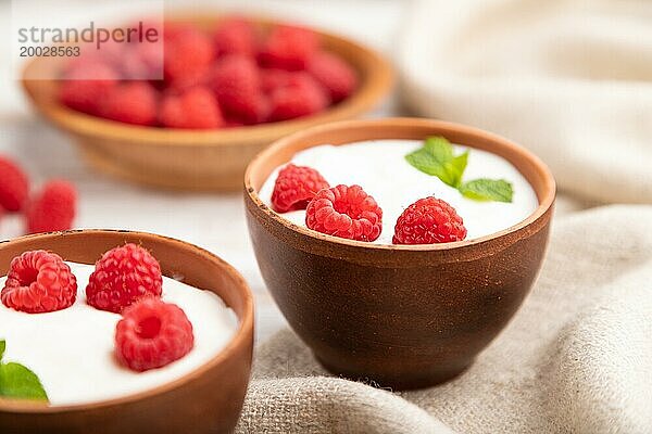 Joghurt mit Himbeeren in Tonbechern auf weißem Holzhintergrund und Leinentuch. Seitenansicht  Nahaufnahme  selektiver Fokus