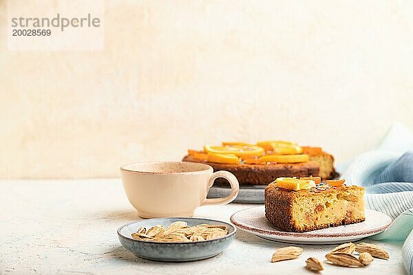 Orangenkuchen mit Mandeln und einer Tasse Kaffee auf einem weißen Betonhintergrund und blauem Leinentuch. Draufsicht  Kopierraum  selektiver Fokus