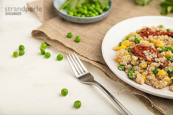 Quinoa Brei mit grünen Erbsen  Mais und getrockneten Tomaten auf einem Keramikteller auf weißem Holzhintergrund und Leinentuch. Seitenansicht  Nahaufnahme  selektiver Fokus