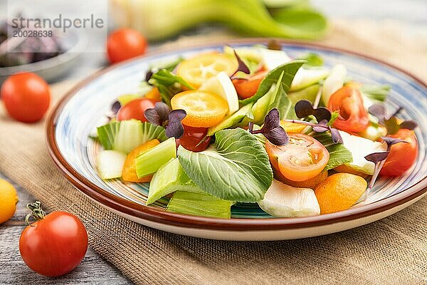 Vegetarischer Salat aus Pac Choi Kohl  Kiwi  Tomaten  Kumquat  Mikrogrünsprossen auf grauem Holzhintergrund und Leinentuch. Seitenansicht  Nahaufnahme  selektiver Fokus