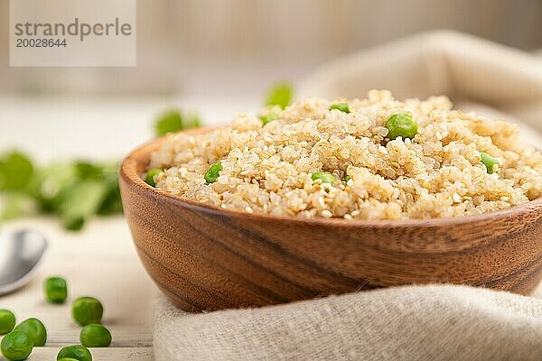 Quinoa Brei mit grüner Erbse in einer Holzschale auf weißem Holzhintergrund und Leinenstoff. Seitenansicht  Nahaufnahme  selektiver Fokus